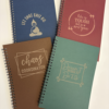Set of custom spiral journals in assorted colours with engraved motivational sayings on the covers.